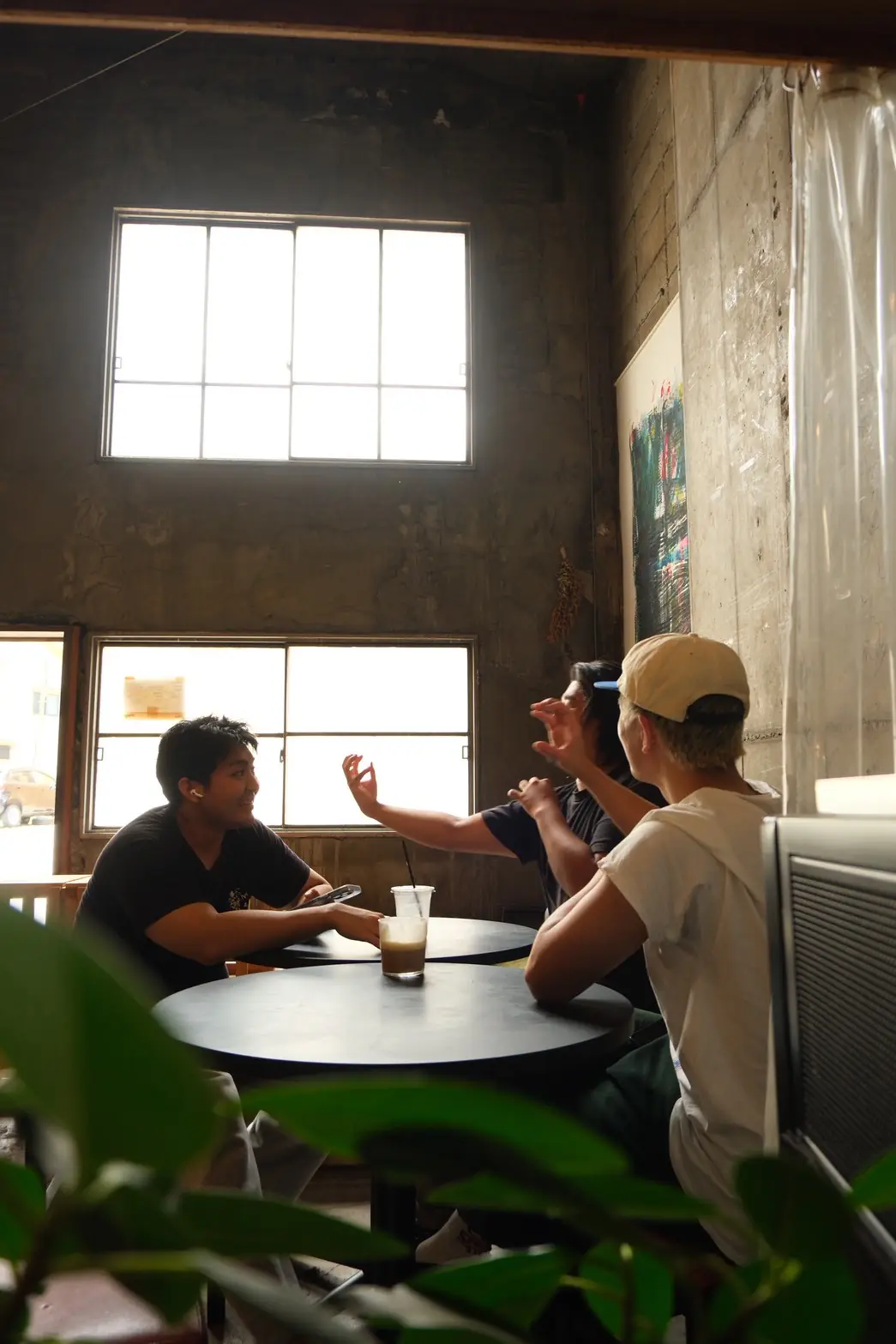 TUMUGU COFFEE STANDの高い天井の店内で、テーブルを囲んで会話を楽しむお客さまたち